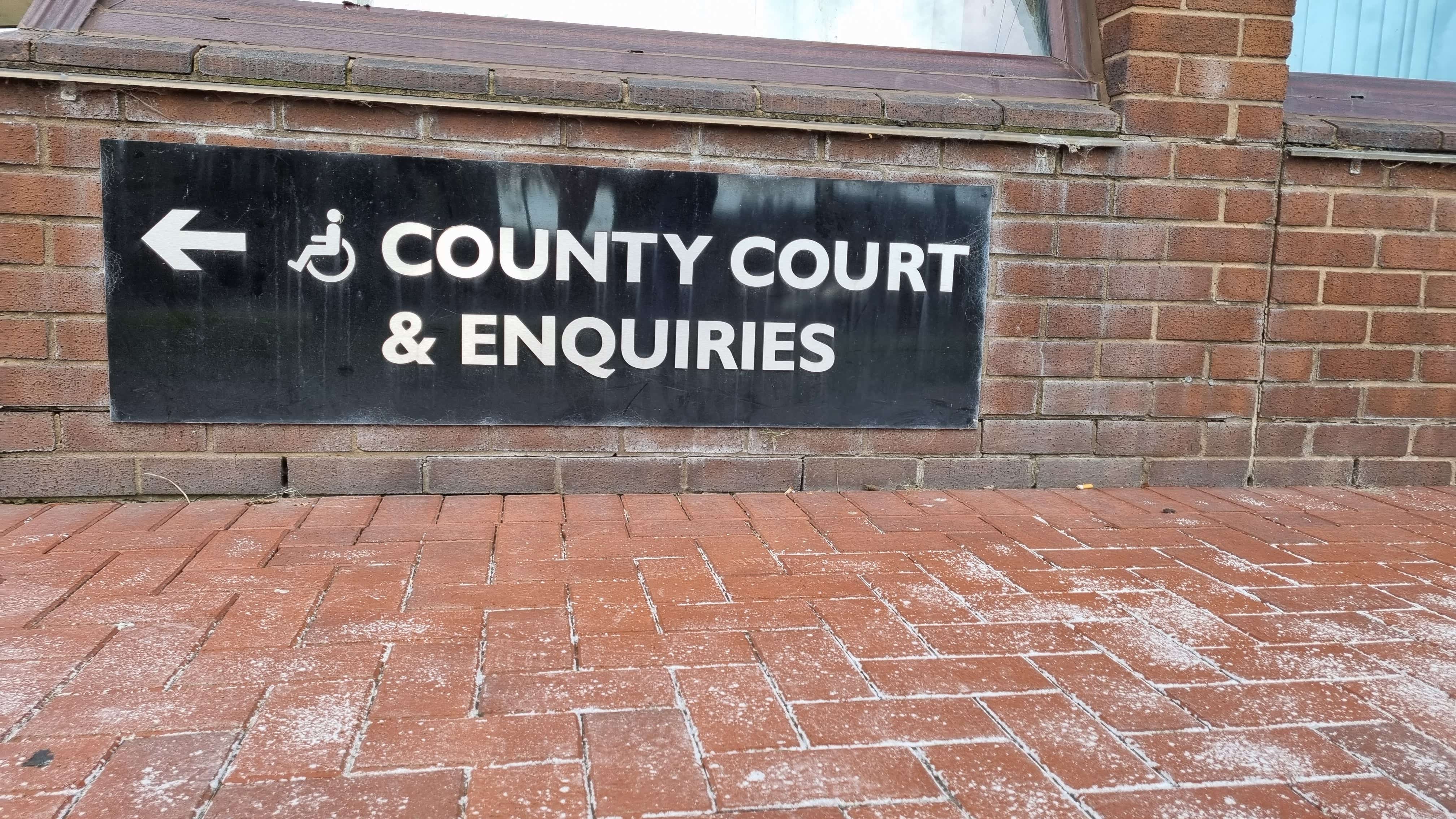 sign reading: County Court and Enquiries with an arrow and wheelchair accessible sign against a brick wall