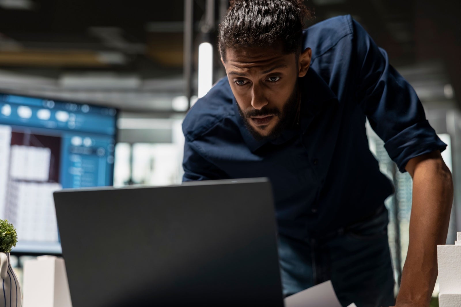 Businessman standing at his desk and leaning down to use his laptop