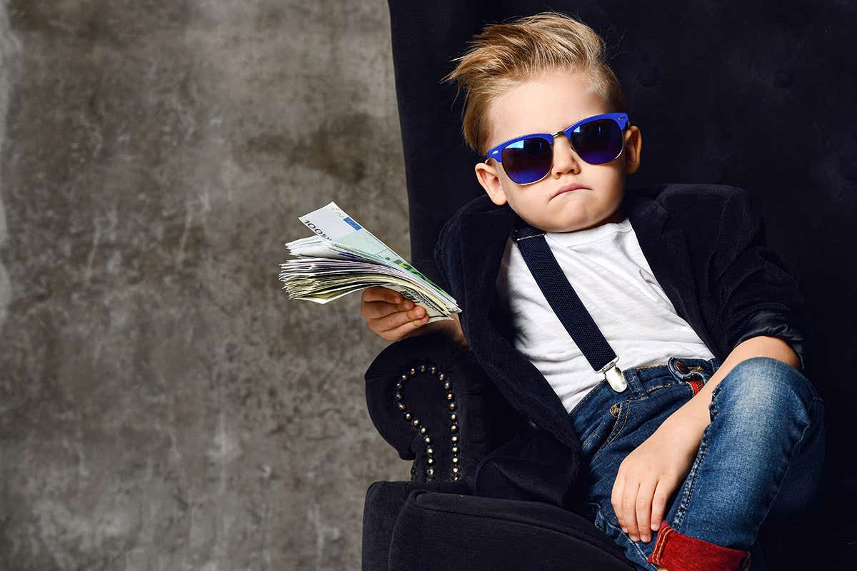 A toddler, dressed in a suit, carrying a load of cash