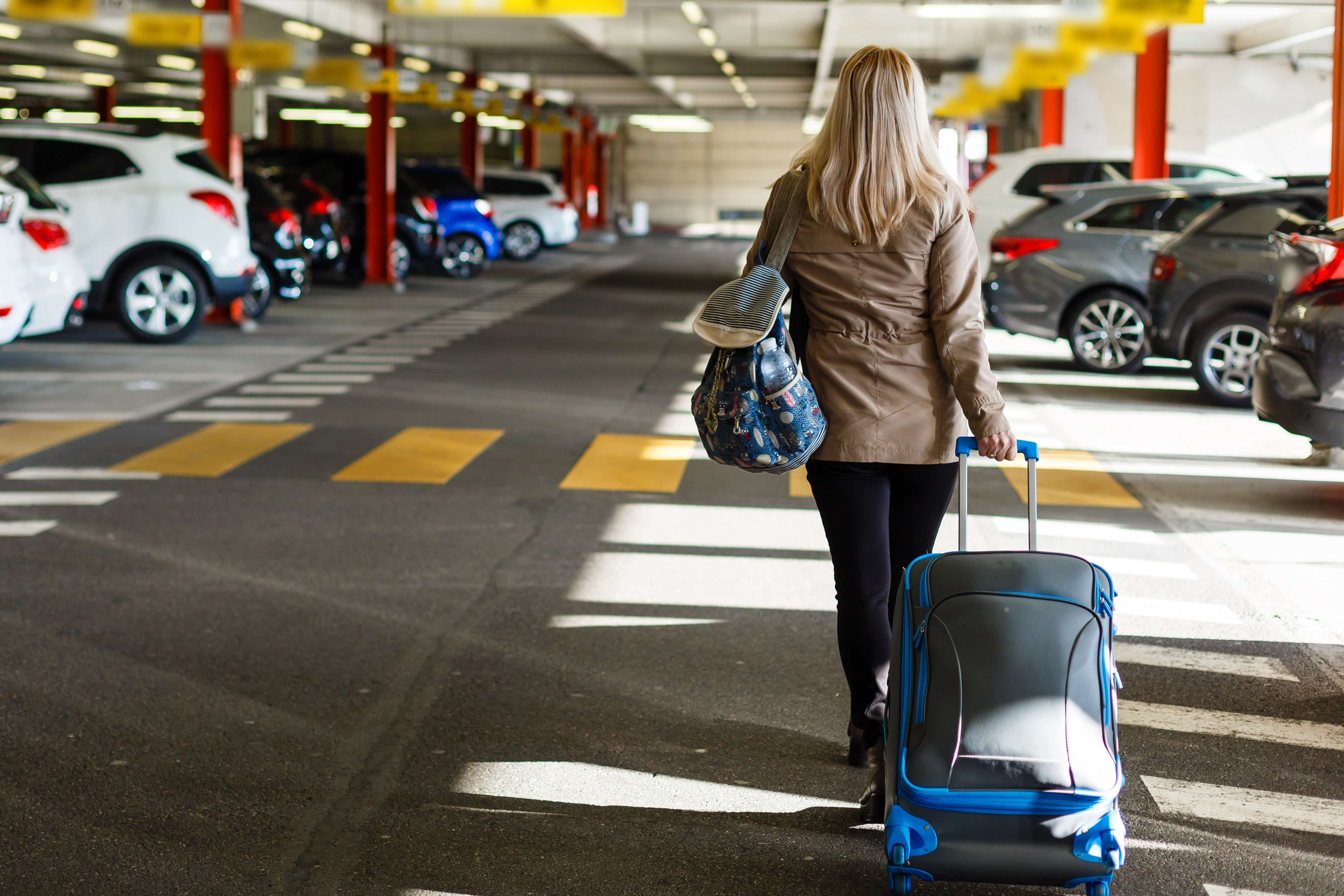A woman heads to the terminal with her luggage after parking her car at the airport