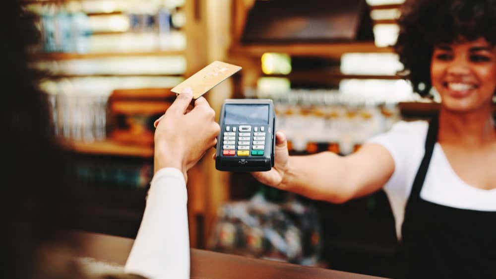 A woman is holding a credit card and paying on a contactless machine