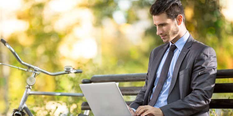 Businessman in a park sitting on a bench on his laptop