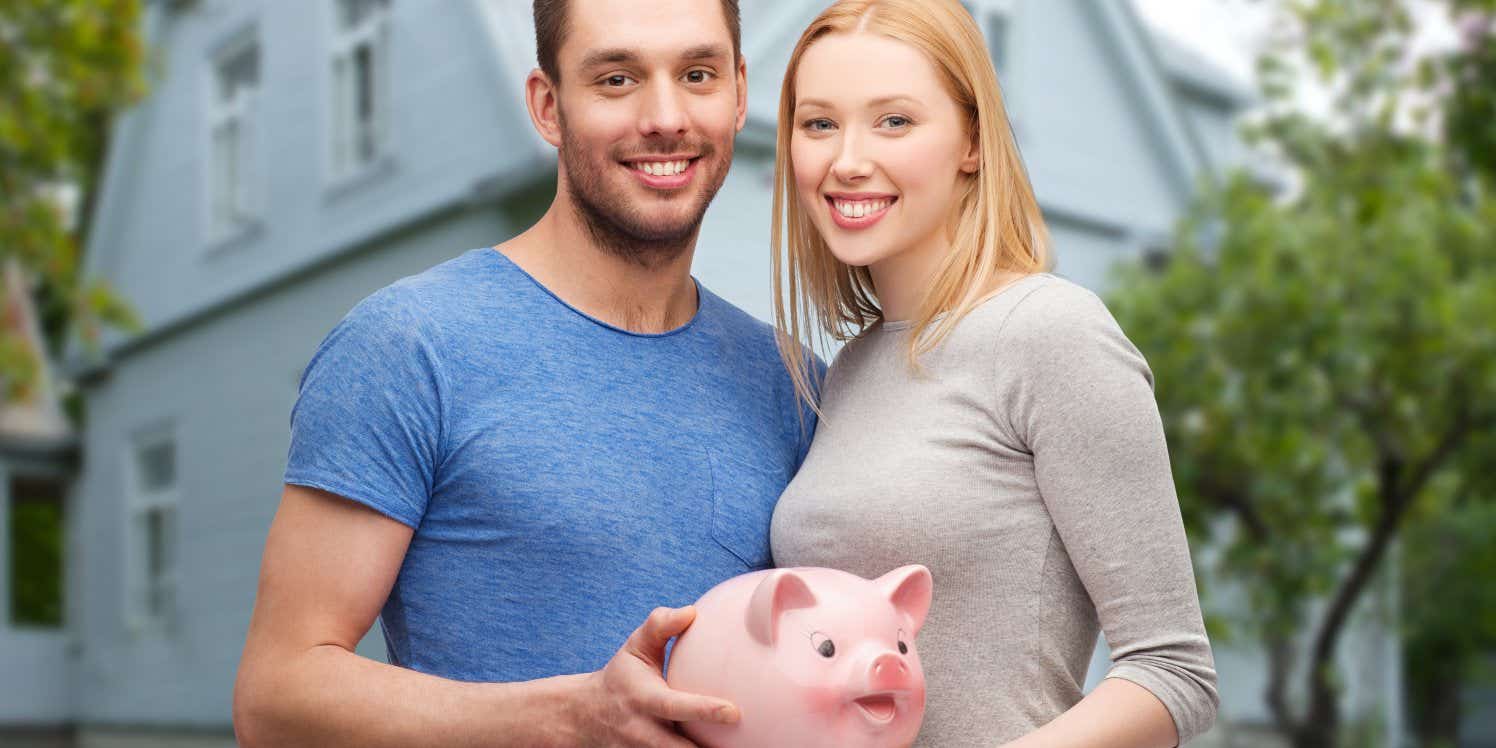 Couple holding piggy bank outside house