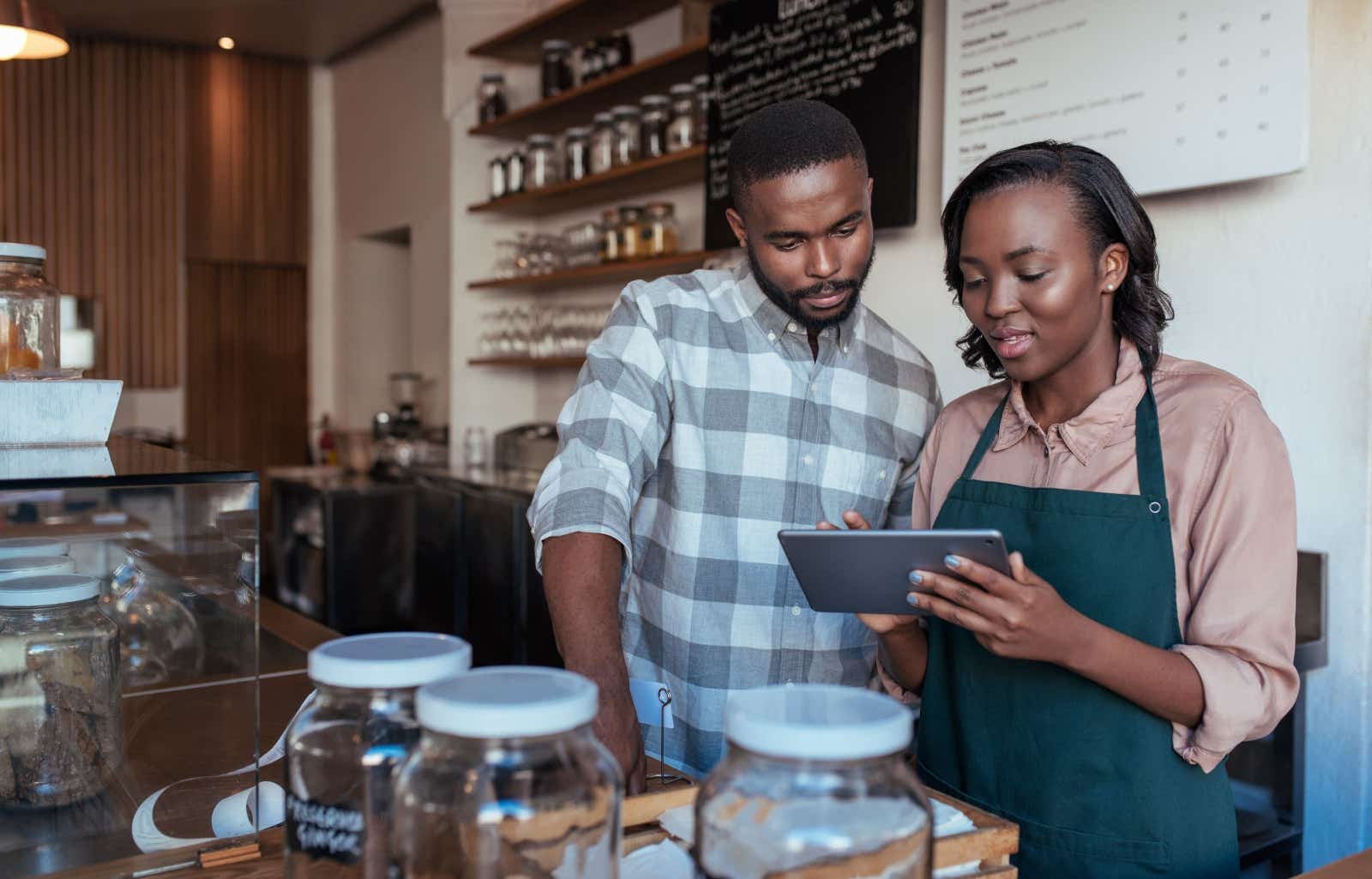 A couple working in a cafe check something on a tablet screen