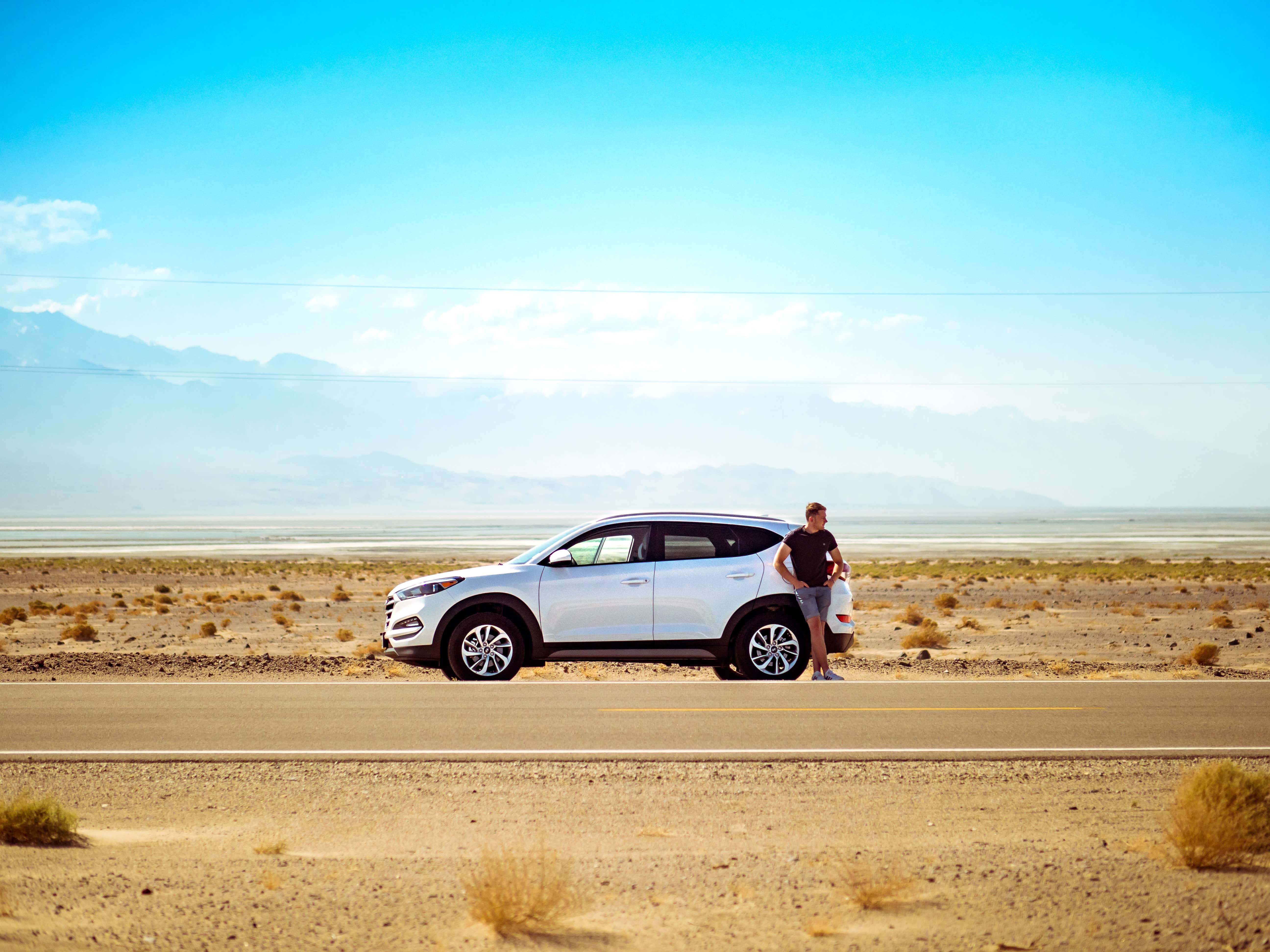 man is standing next to a car in the middle of the desert. 