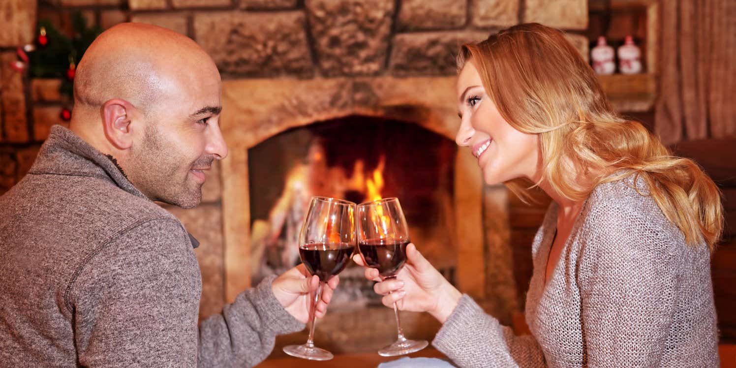 Couple clinking champagne glasses sitting by fireplace