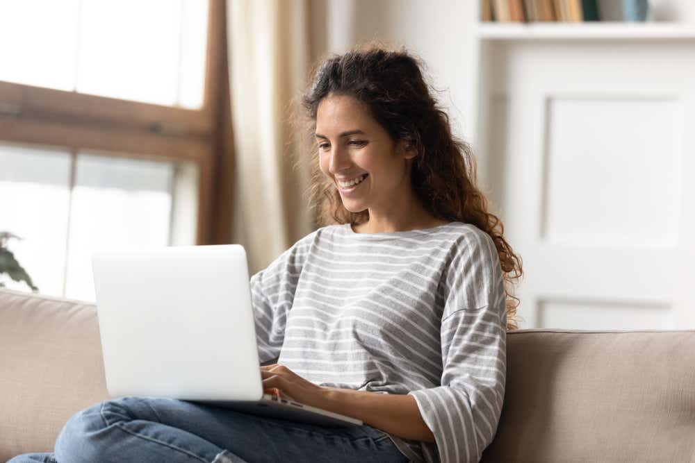 Women sitting on a sofa smiling at a laptop