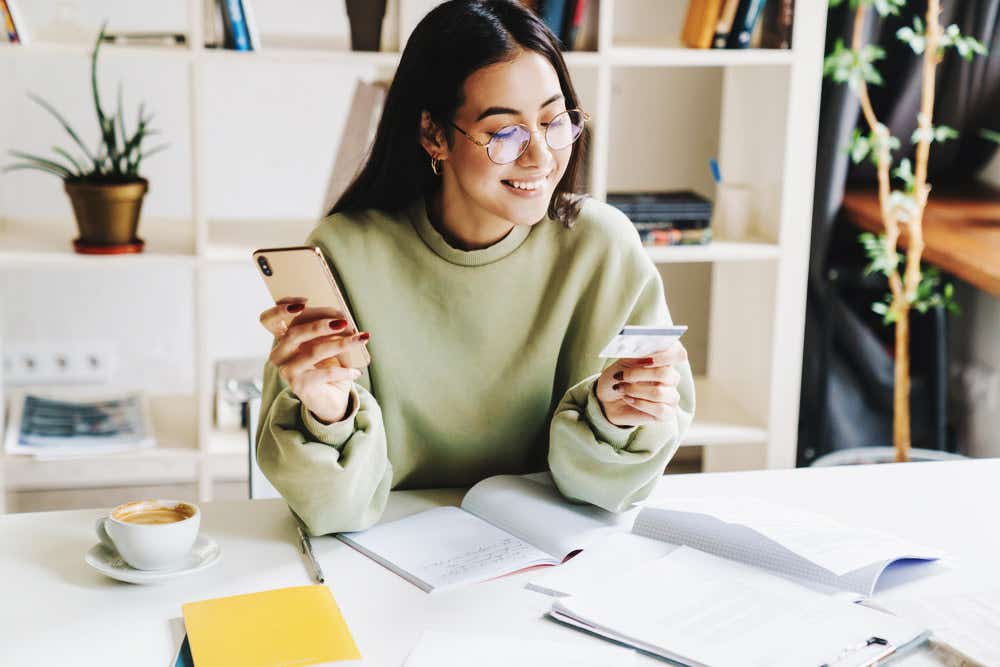 A woman is holding her phone and looking at a credit card