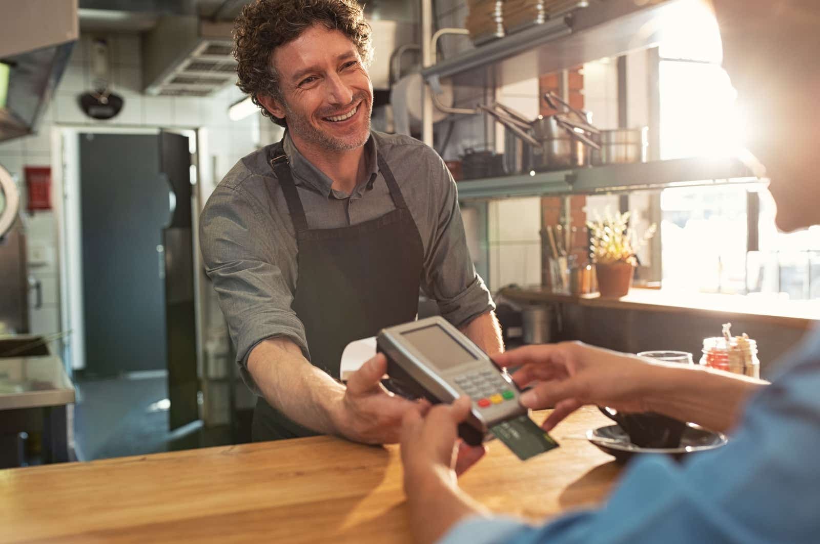 A smiling vendor offers a customer a card payment machine