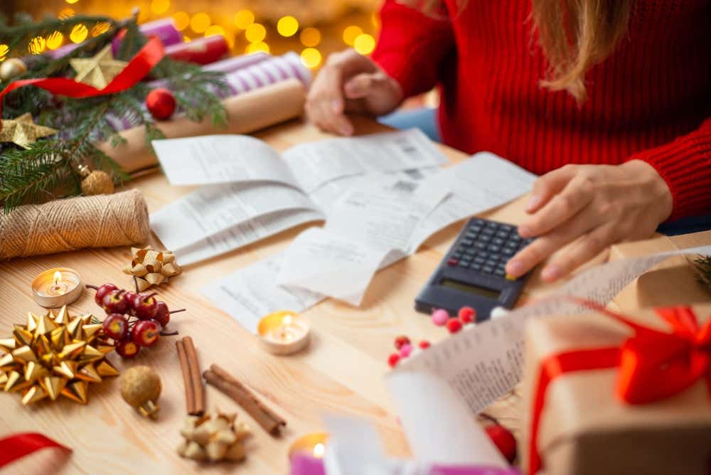 Close up of woman looking at bills and calculator surrounded by Christmas decorations. 