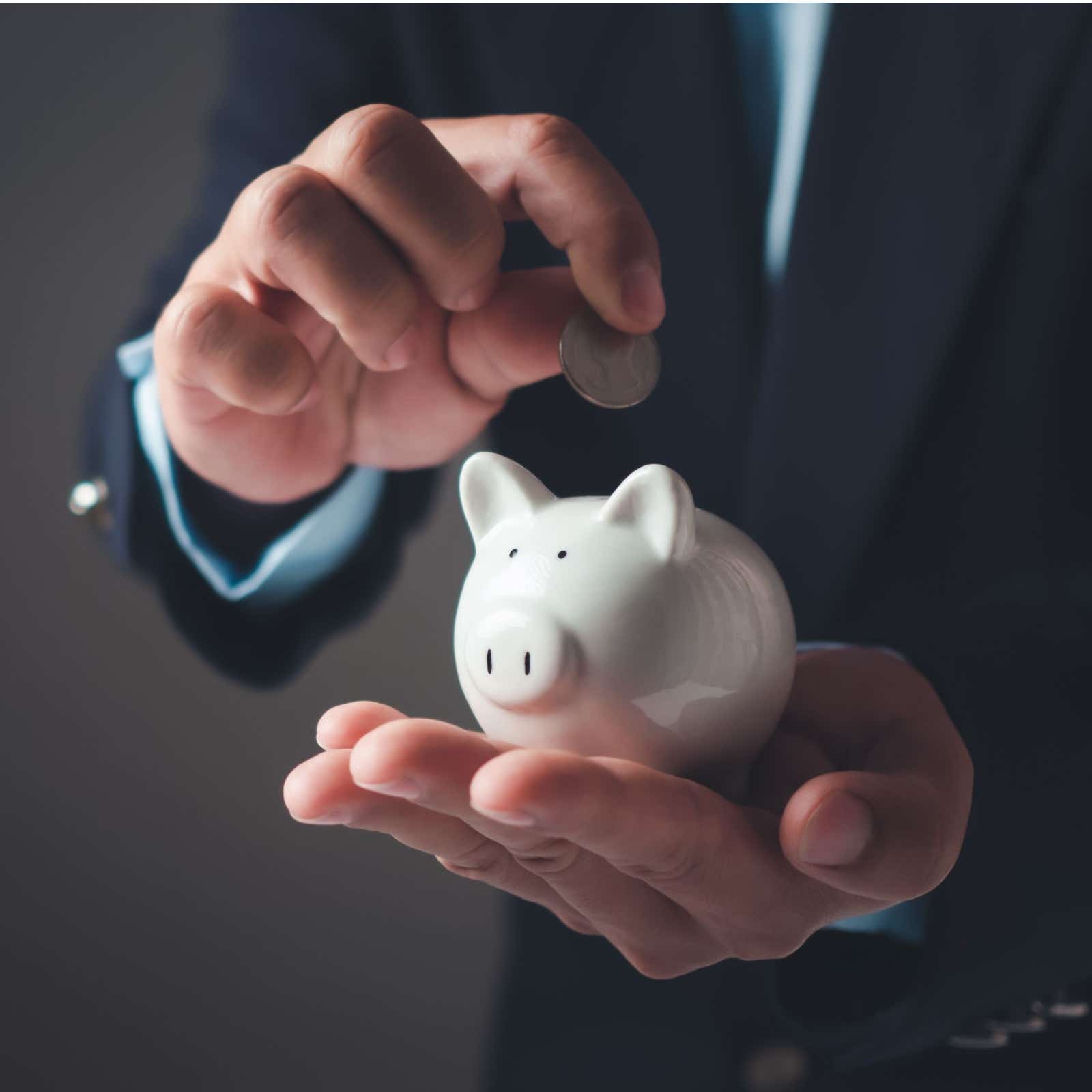Man in business suit holding piggy bank and dropping in money