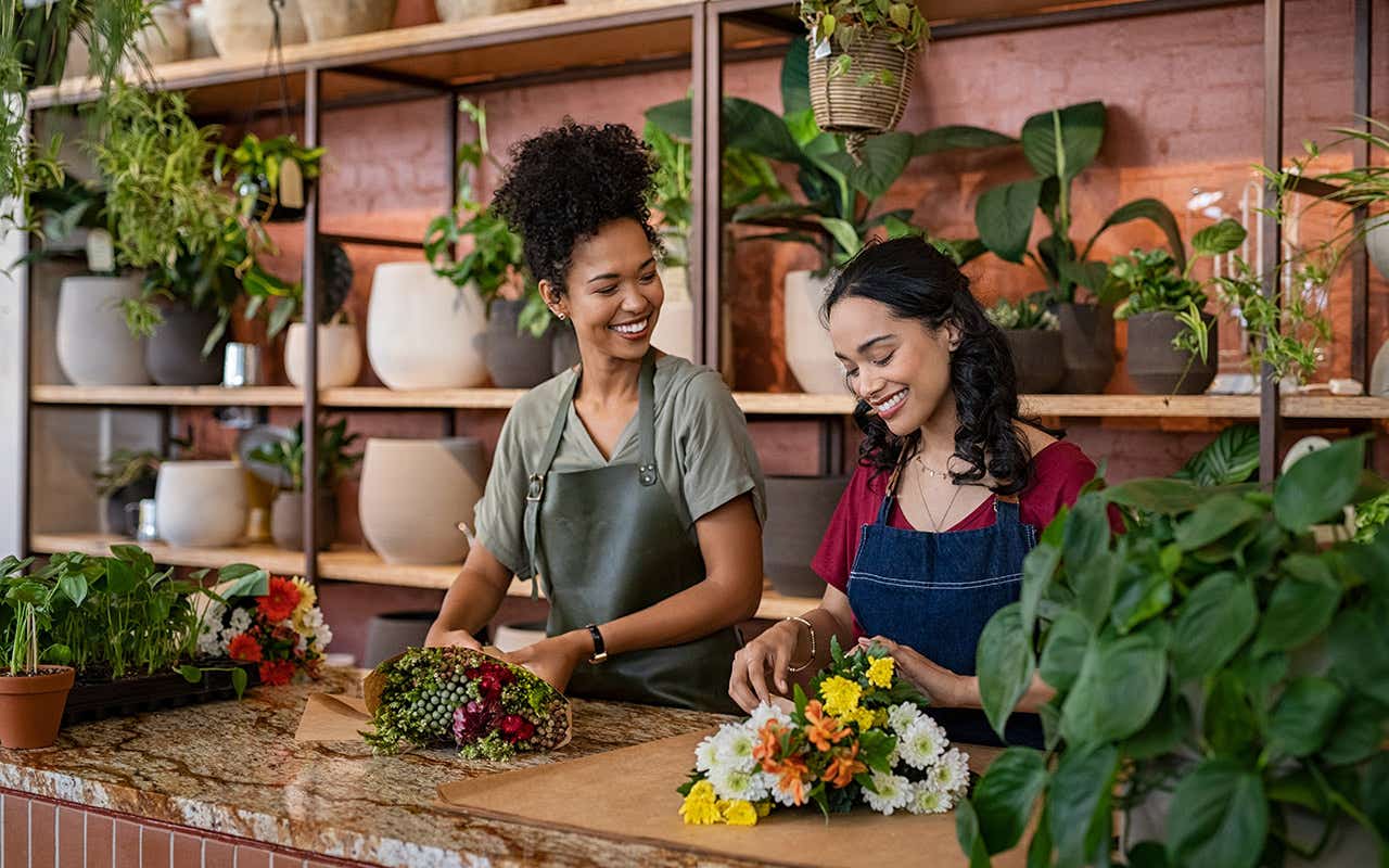 Two happy and smiling young woman florist working together in flower shop.