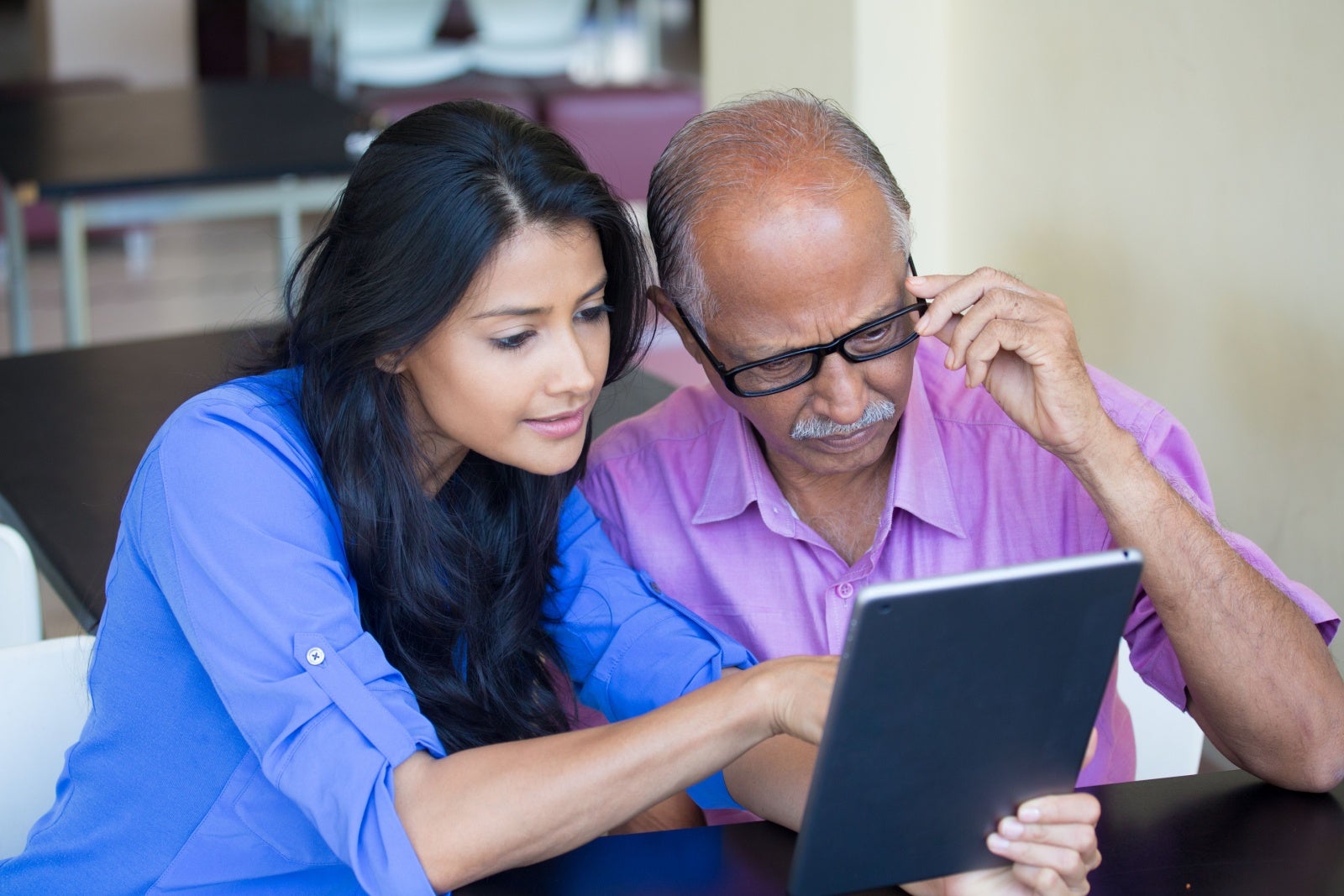 A father and his adult daughter sit together reading a tablet.