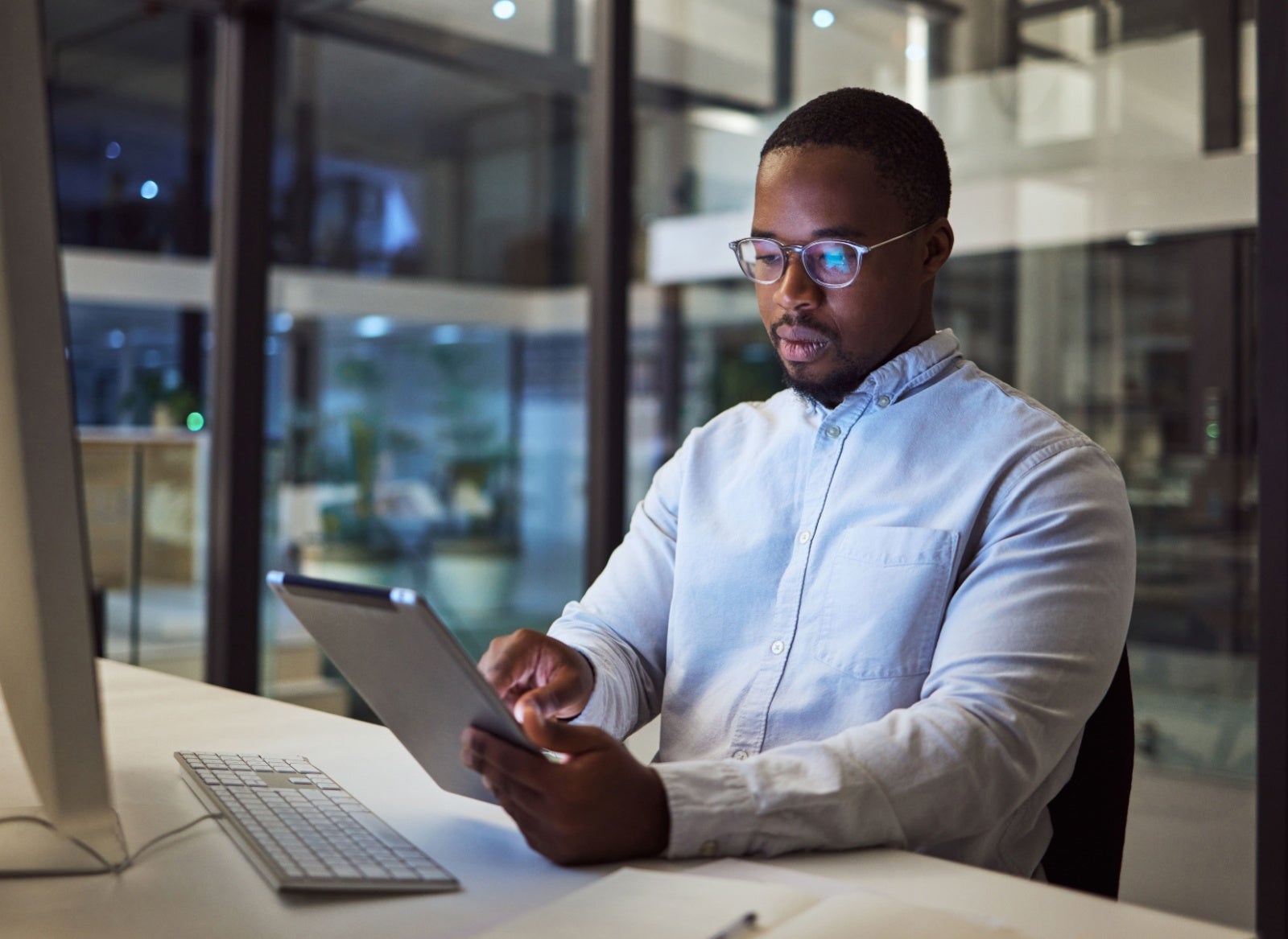 Businessman focusing on his tablet, while sitting at his desk in the evening