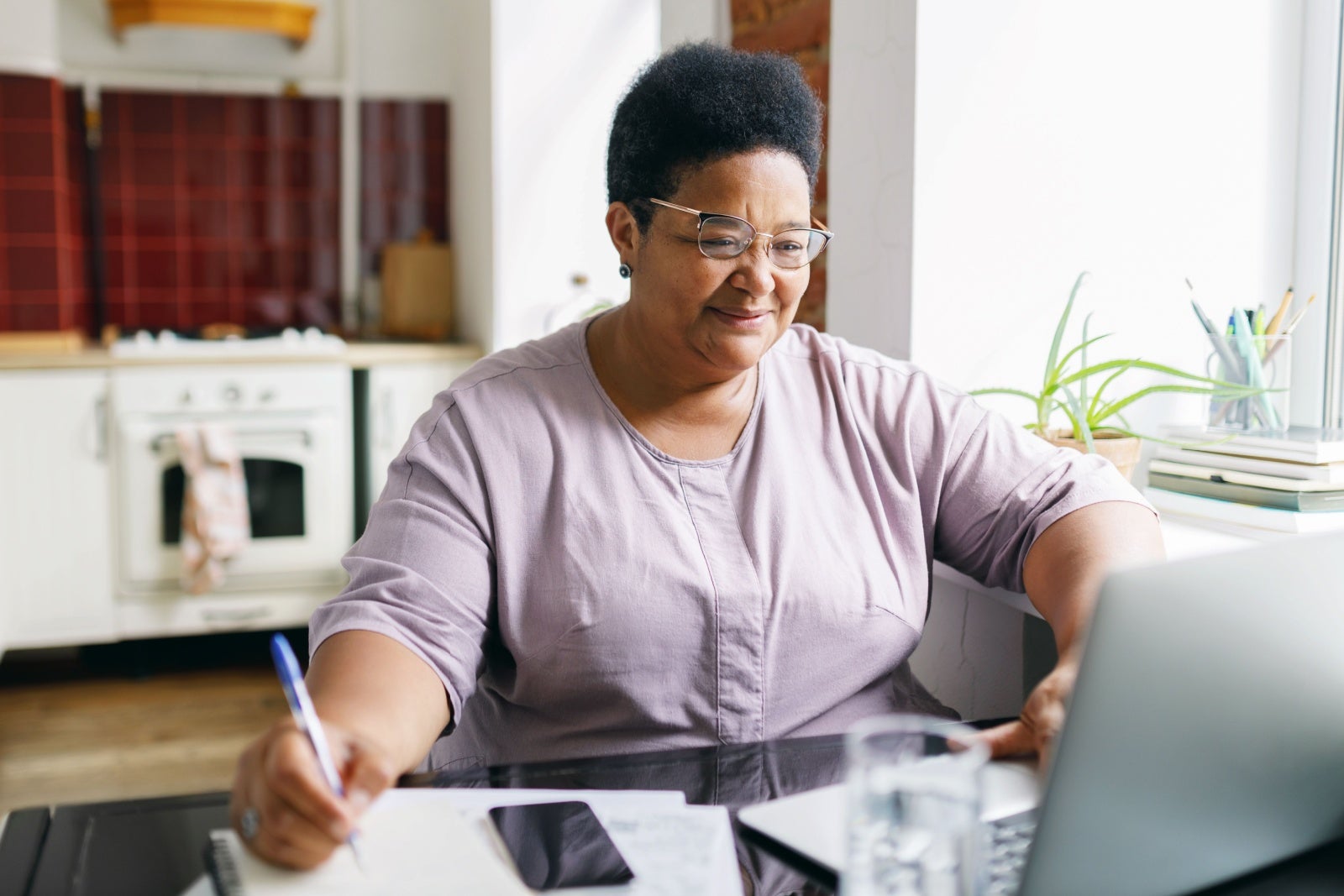 A woman takes notes while looking at a laptop screen.