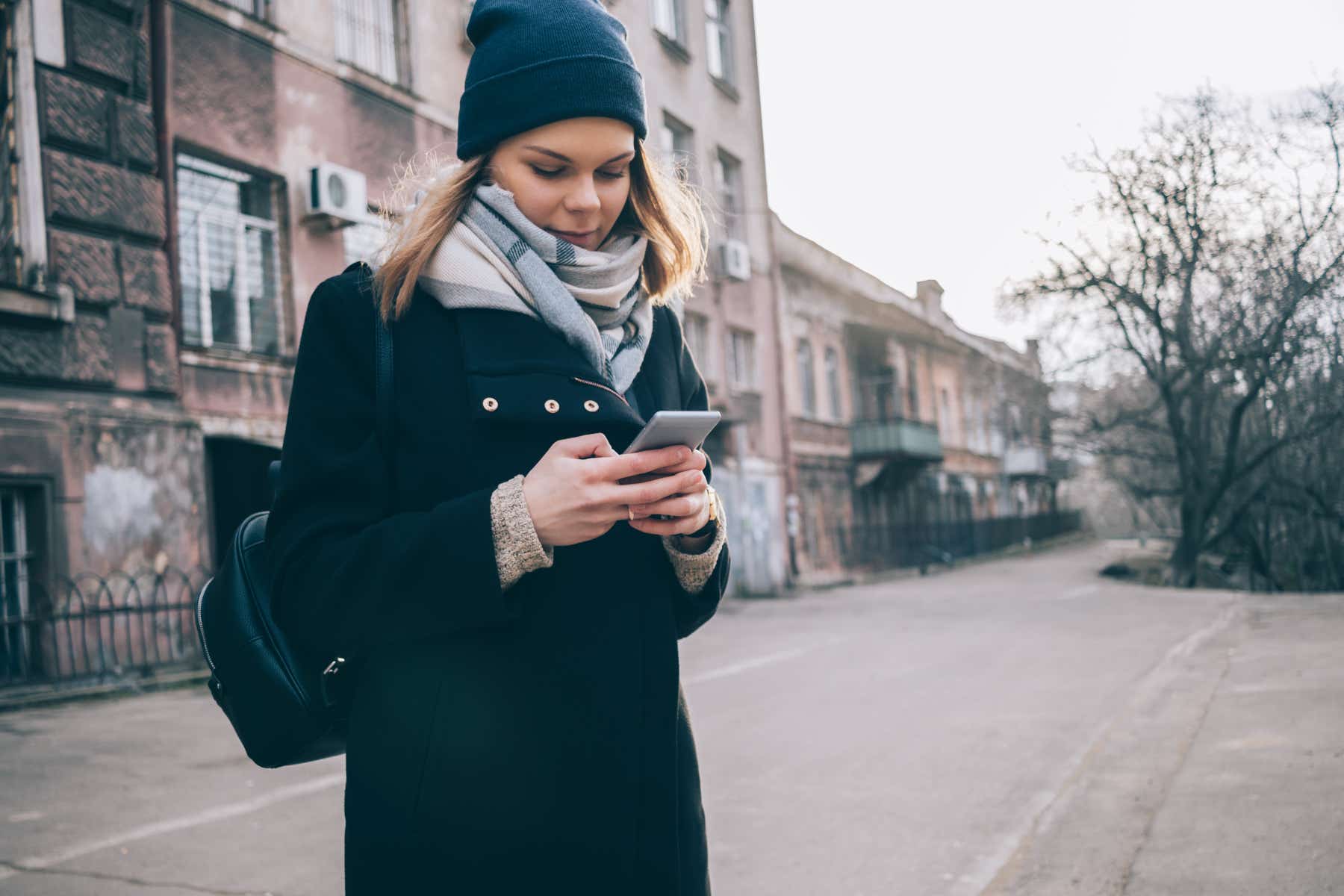 Woman in coat, hat and scarf looking at her smartphone