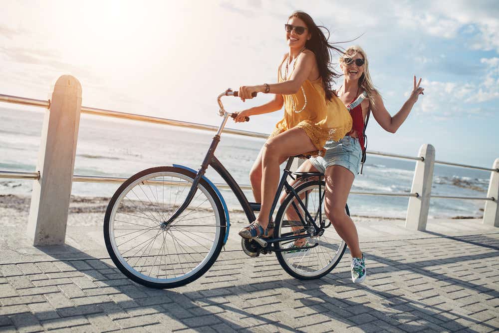 Two women on a bike cycling along the coast in the sunshine. 