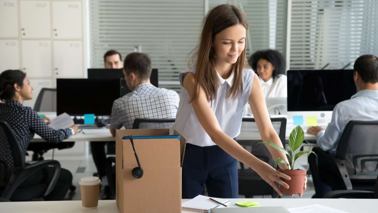 Smiling hired female company employee unpacking box with personal belongings