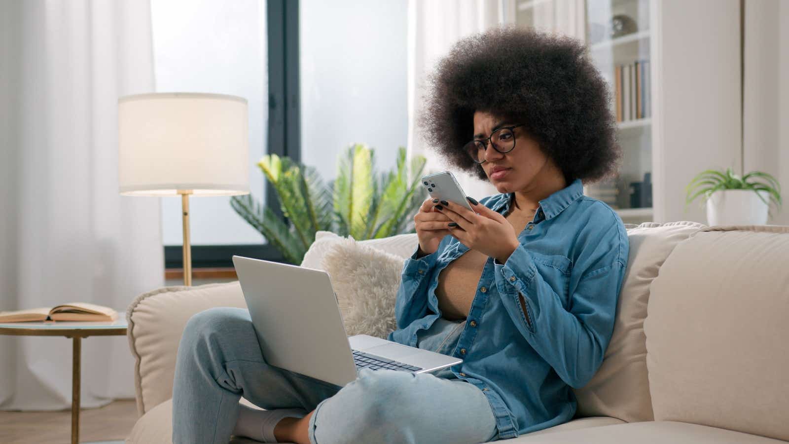 Confused-looking woman using a laptop and smartphone