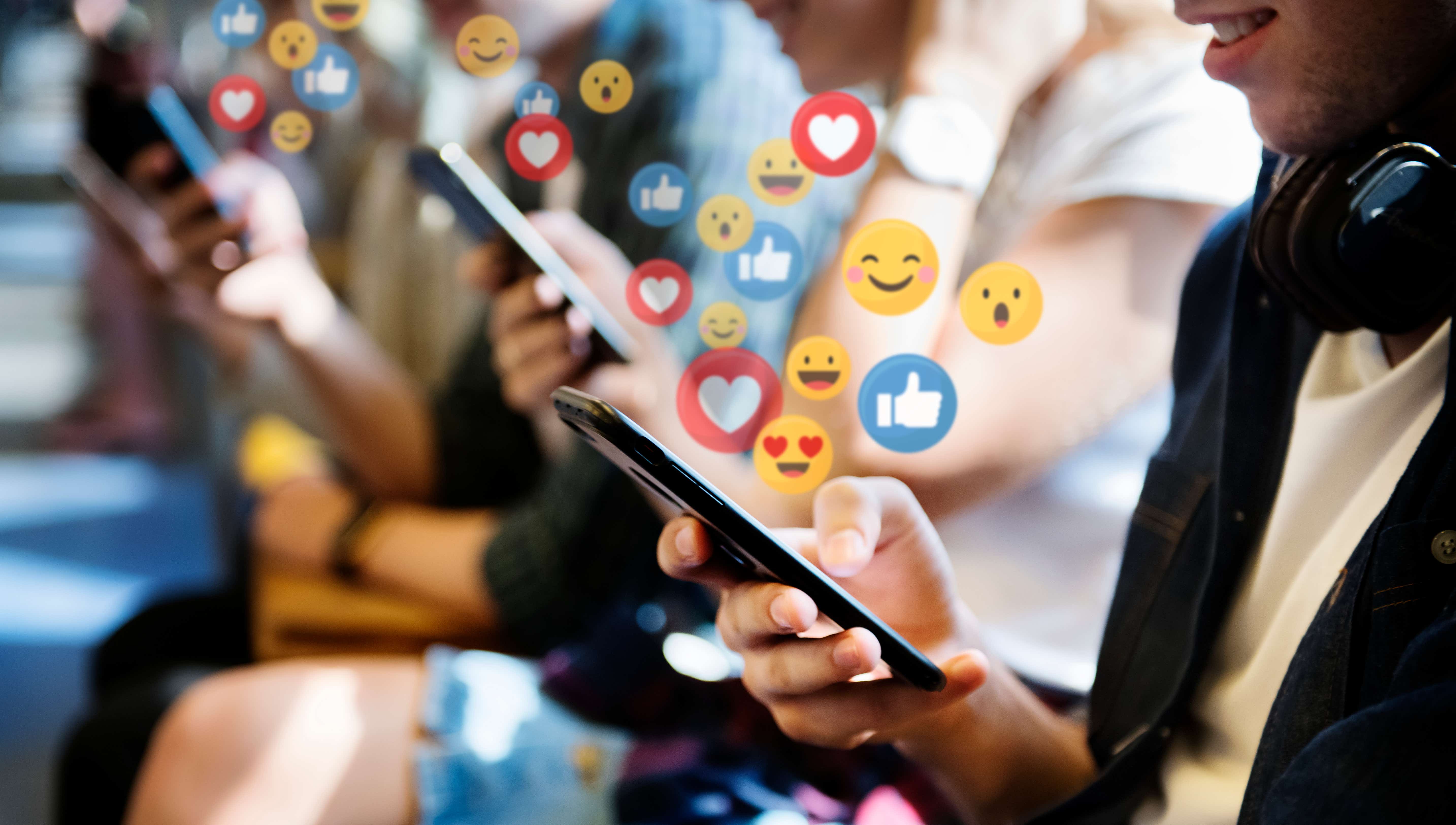 Group of people looking at phones with social emojis 