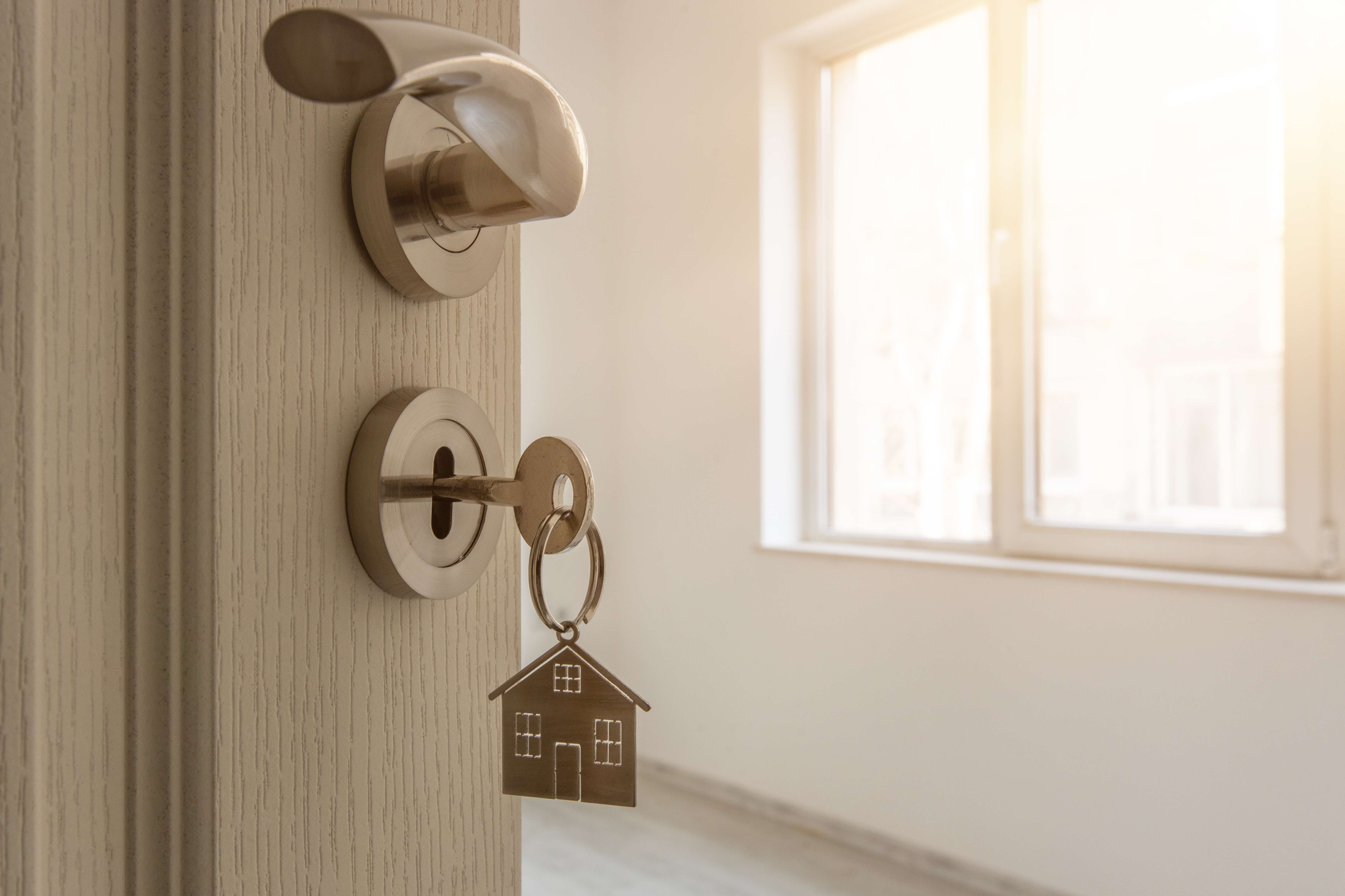 Door opened to a new house with a house-shaped keyring in the lock. 