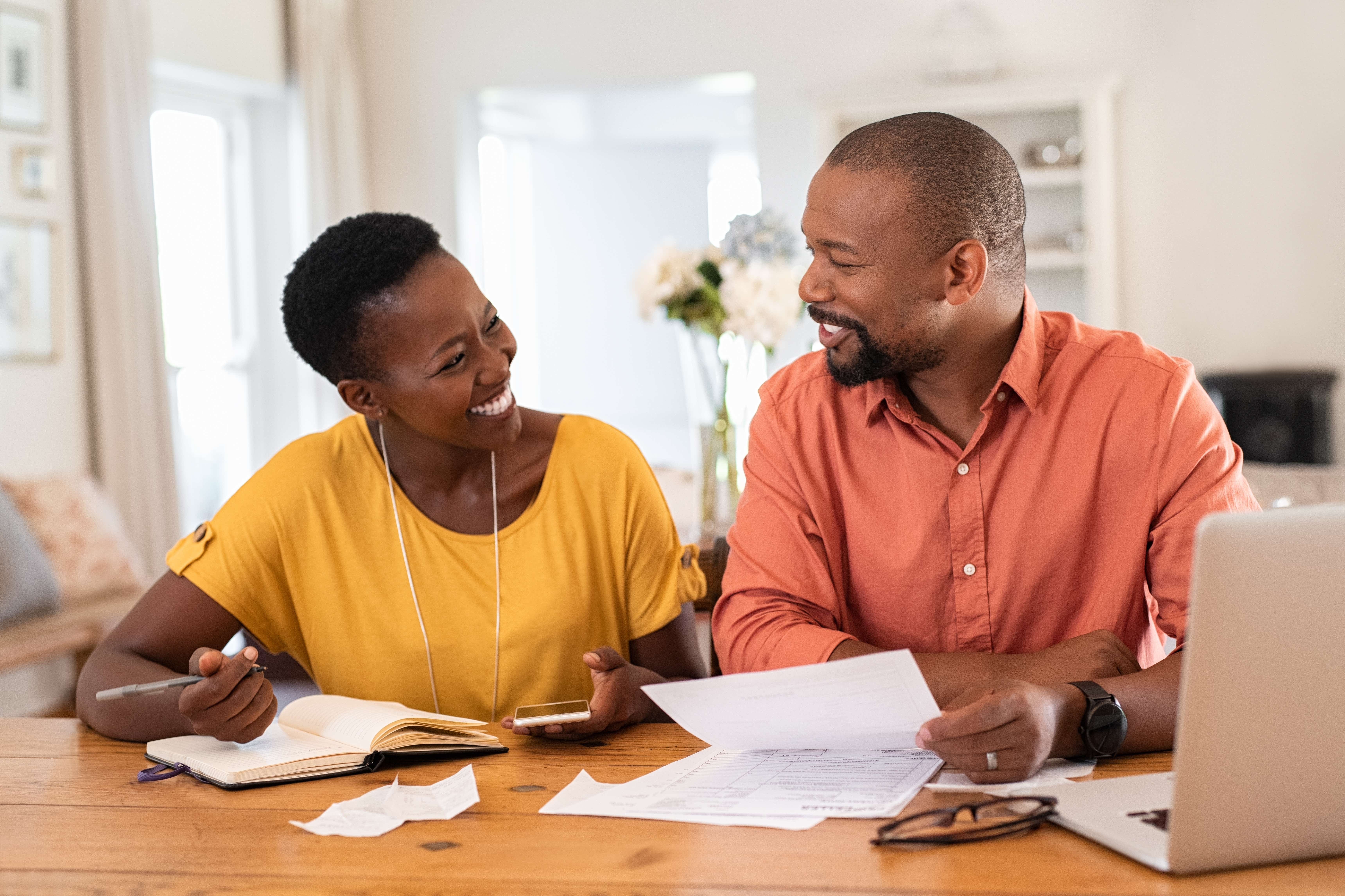Smiling couple sitting together at home looking at bills and paperwork