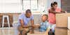 A black family of three, an adult male and female with a young boy are packing boxes to move house. All of them are smiling and there is only a sofa left in the background, with multiple boxes in the foreground of the room