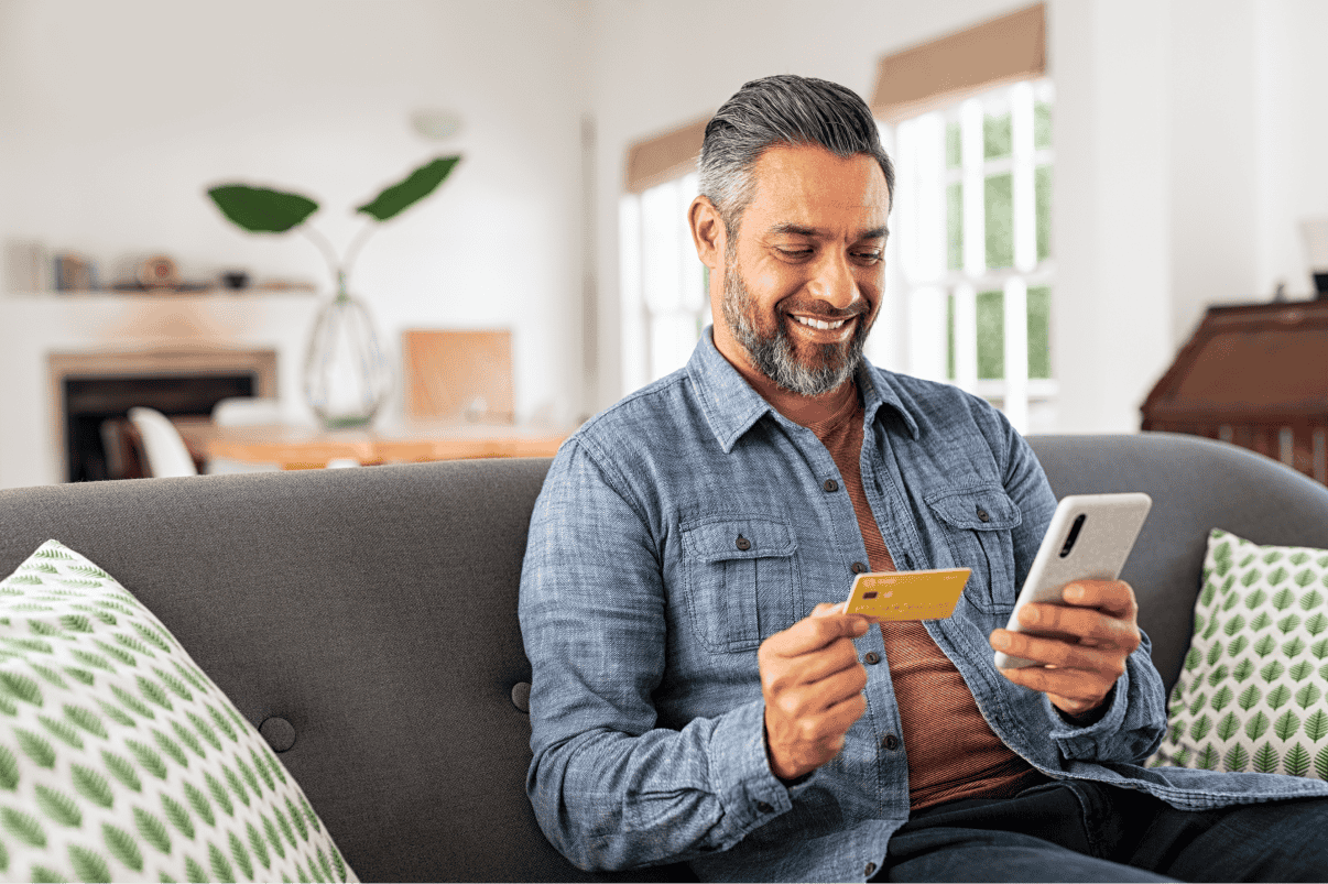Man sitting on sofa looking at credit card and phone
