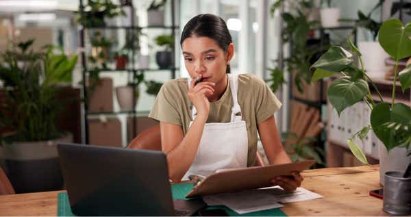 A florist in her shop ponders something on her laptop screen.