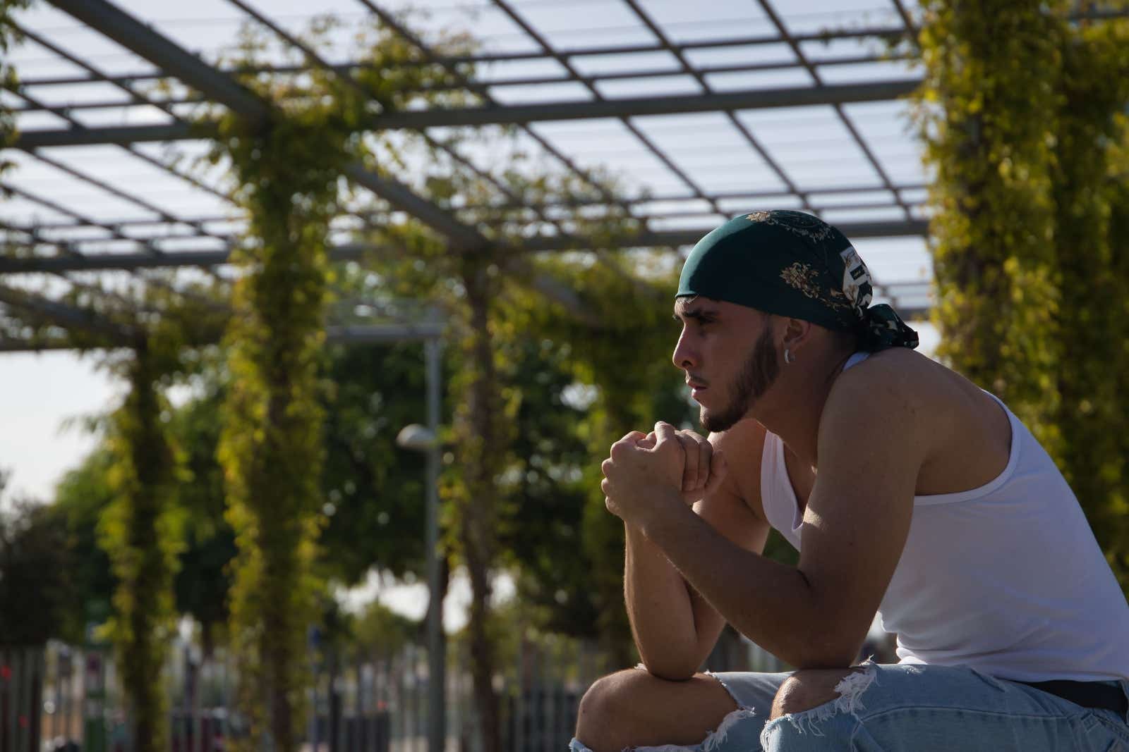 A young man with a bandana on his head seated in a garden