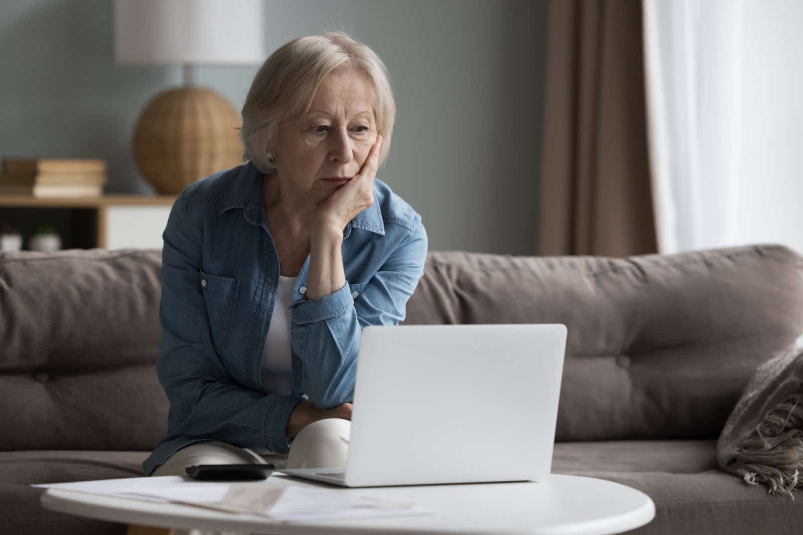 Senior woman looking anxious as she looks at paperwork and laptop screen