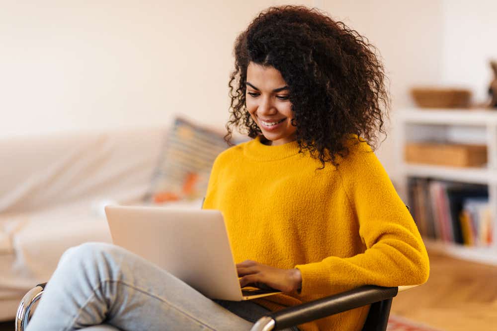 Women is sitting on a chair smiling and looking at her laptop. 