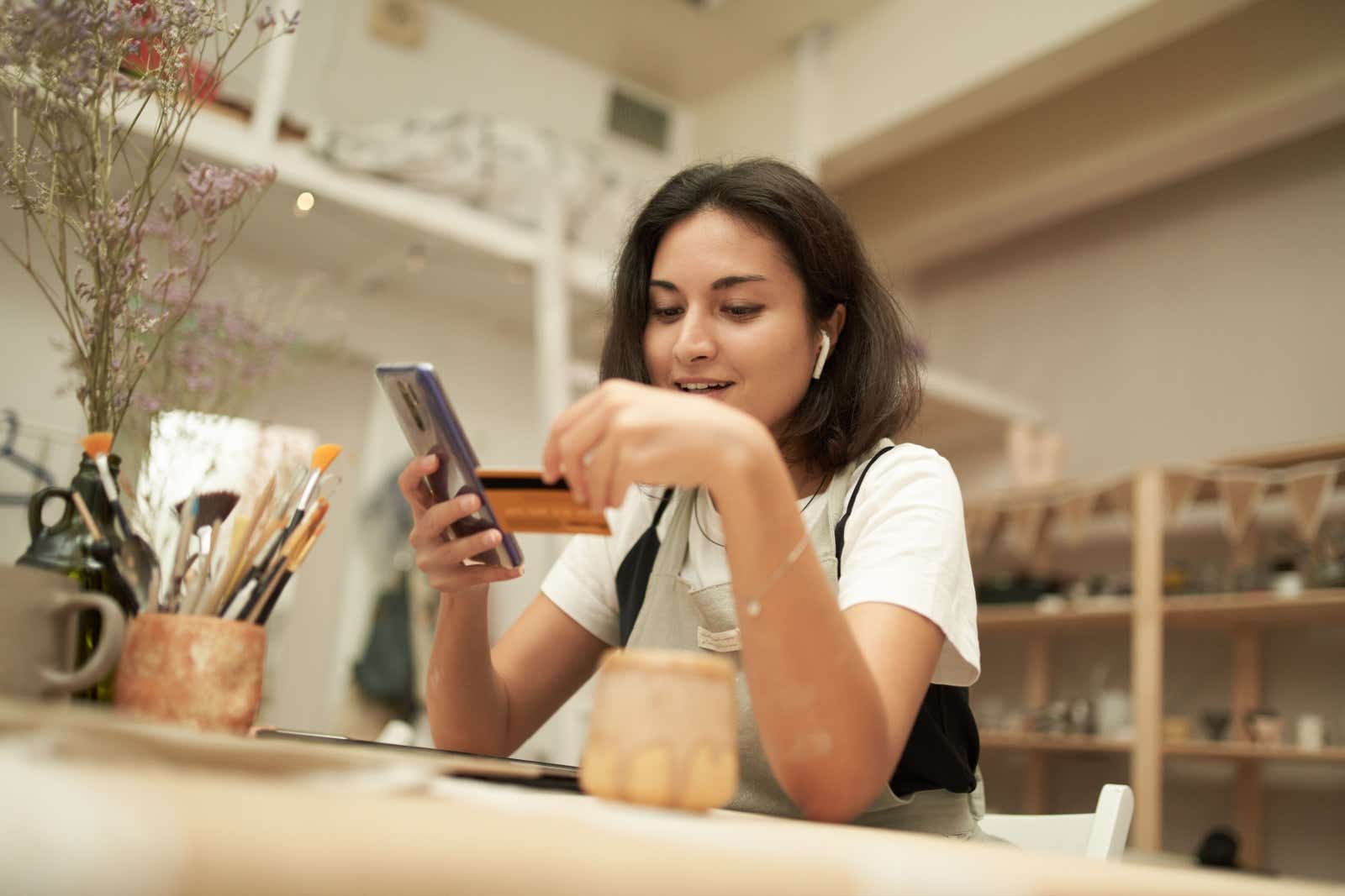 Potter in her workshop entering her credit card details into her smartphone