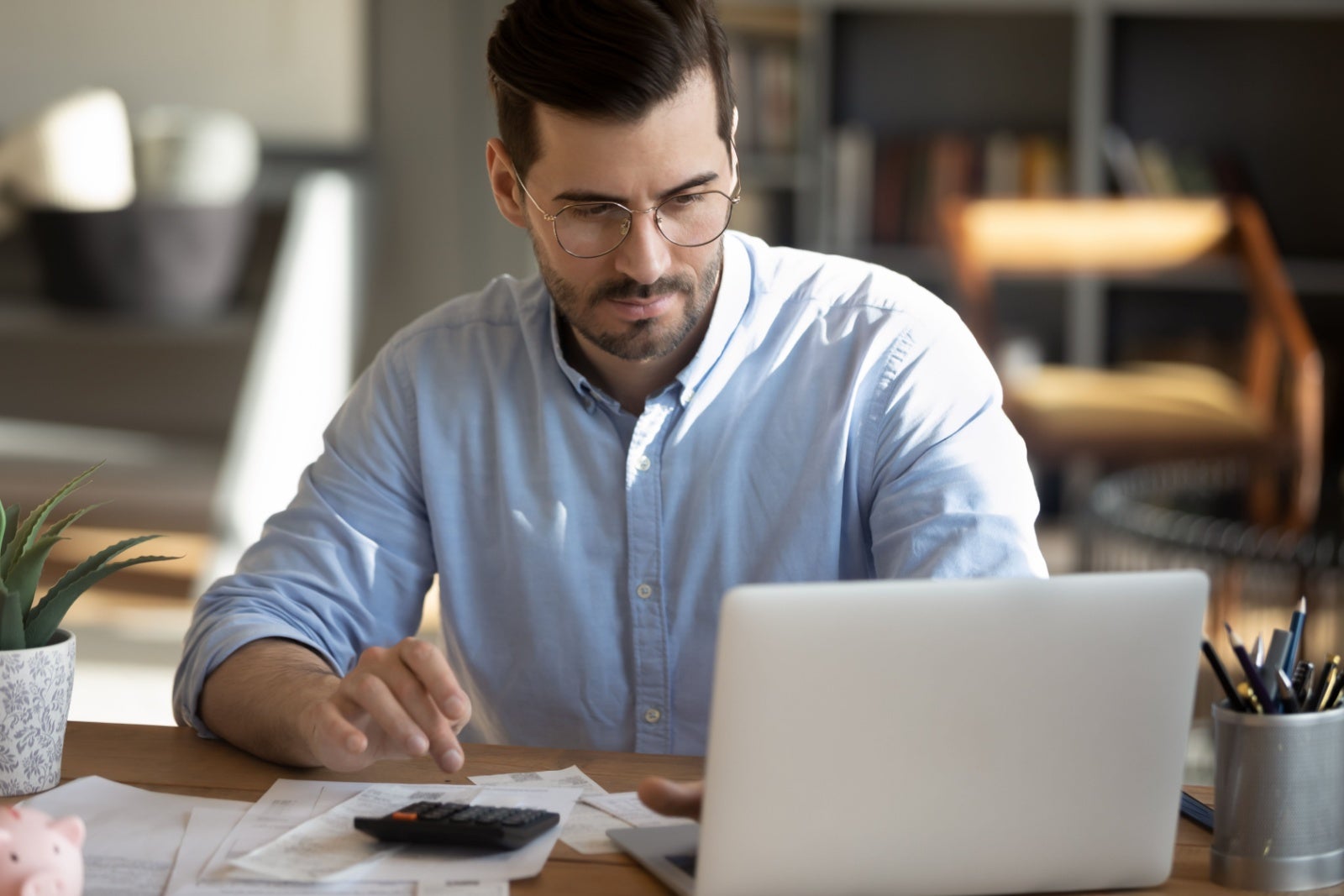 Focused businessman looks at his screen while keying in numbers on a desk calculator