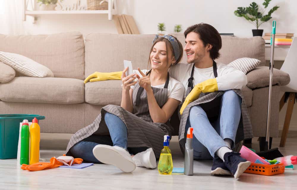 Man and woman sitting on the floor looking at phone surrounded by cleaning products 