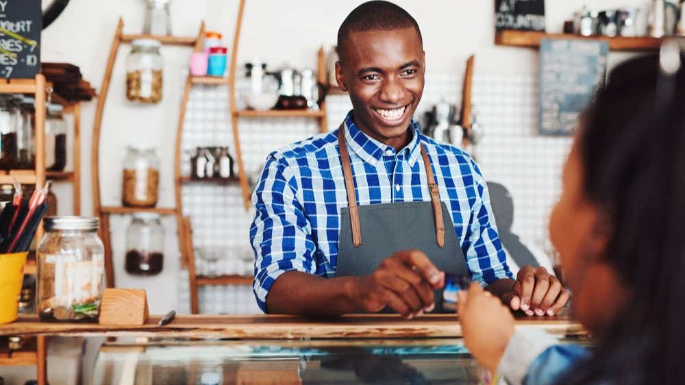 A man is serving a customer in a cafe and taking her credit card for payment