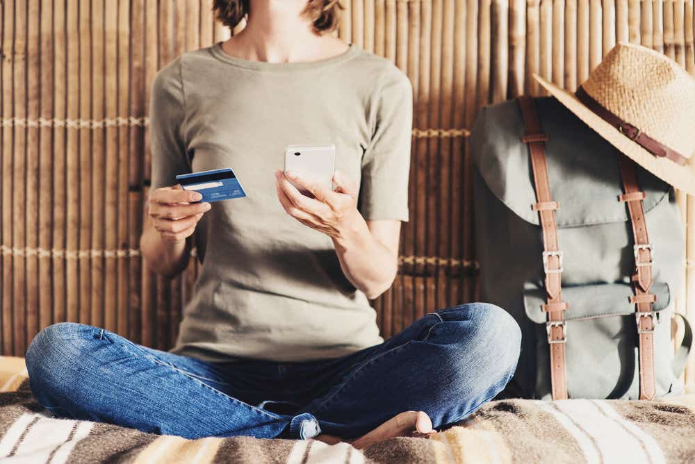 A woman is holding her credit card and phone and she has a packed bag next to her