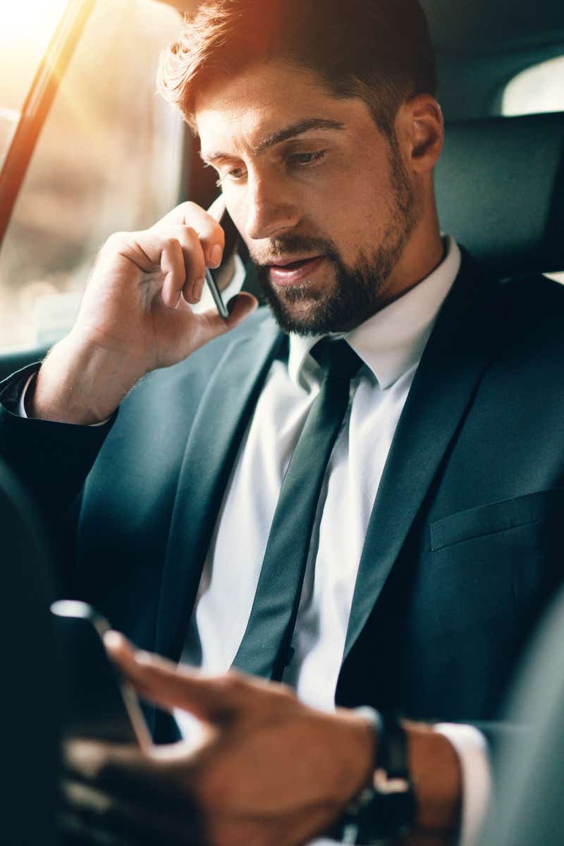 Businessman in a suit and tie on a phone in the back of a car. 