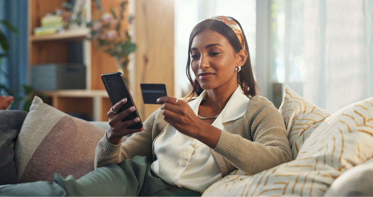 Woman sitting on a sofa looking at a phone and credit card. 