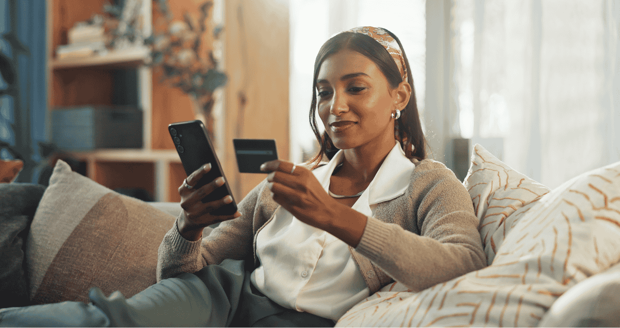 Woman sitting on a sofa looking at a phone and credit card. 